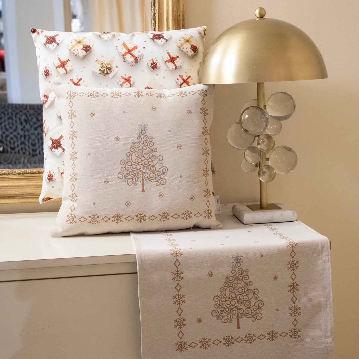 Tischband und Kissen mit stilisiertem Weihnachtsbaum aus goldenen und blauen Wirbeln sowie umgebender Schneeflocken-Borte auf einer Kommode