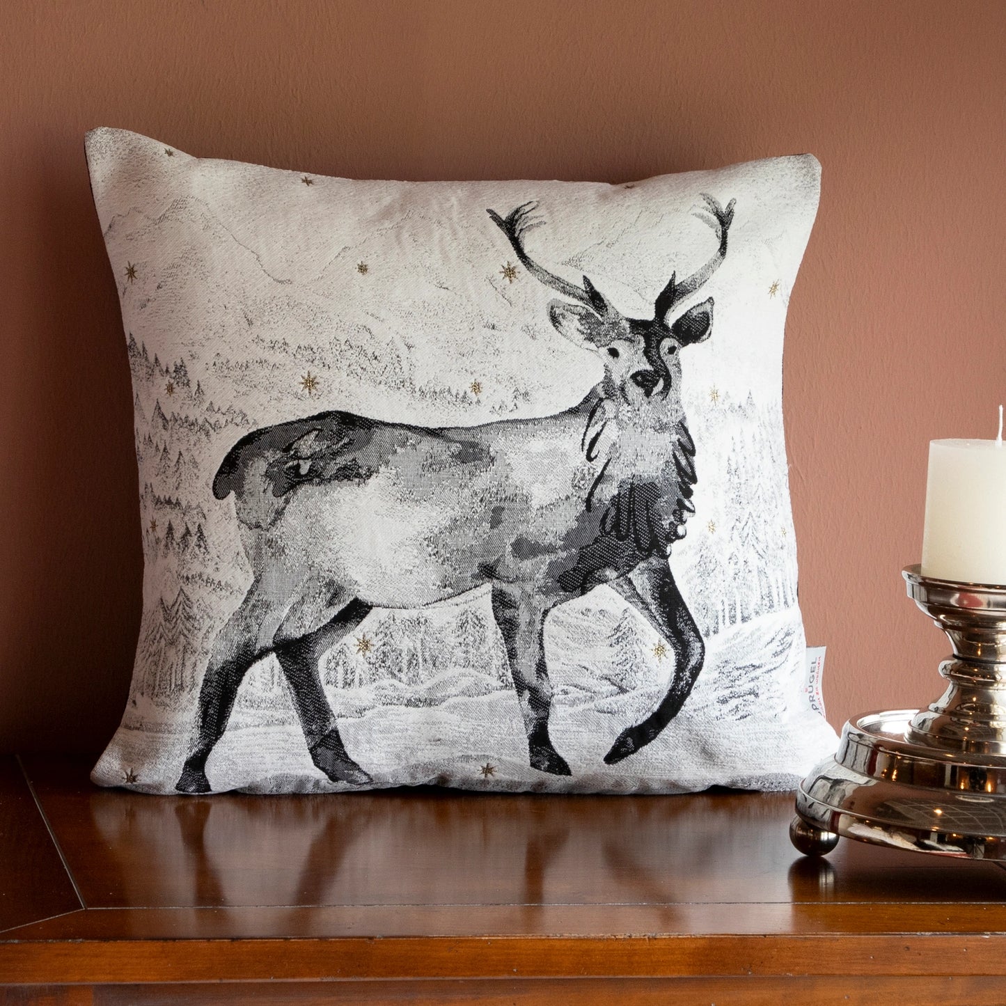 Quadratische Chenille Kissenhülle 45x45 cm in Schwarz-Weiß mit einem majestätischen Hirsch mit Geweih in einer verschneiten Berglandschaft mit funkelnden Sternen auf Holzkommode. 