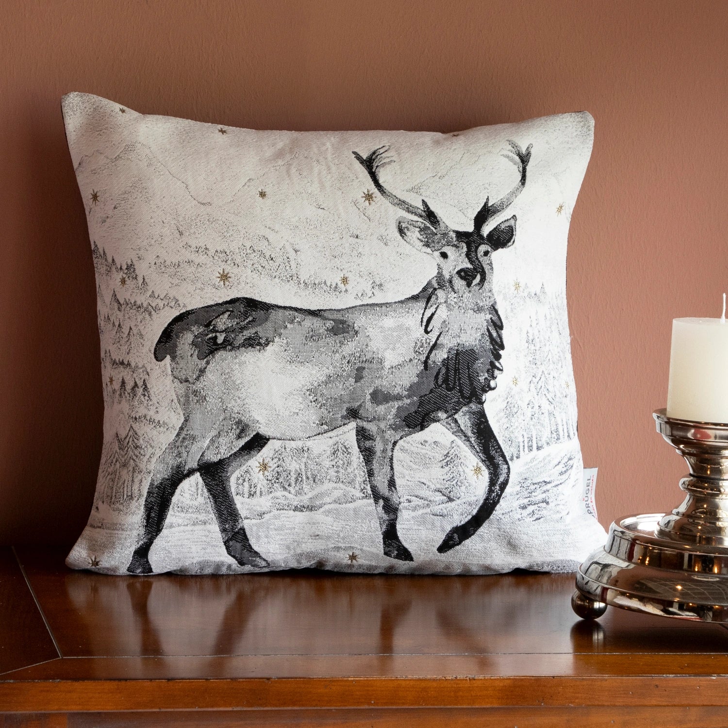 Quadratische Chenille Kissenhülle 45x45 cm in Schwarz-Weiß mit einem majestätischen Hirsch mit Geweih in einer verschneiten Berglandschaft mit funkelnden Sternen auf Holzkommode. 