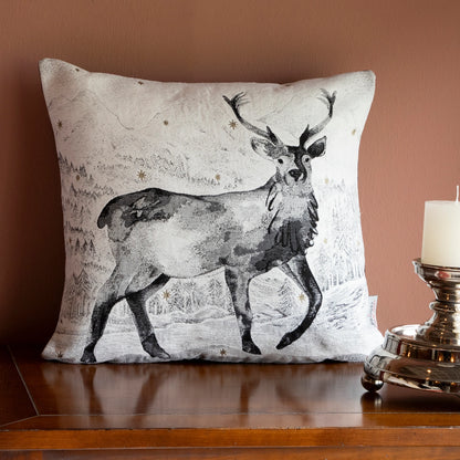 Quadratische Chenille Kissenhülle 45x45 cm in Schwarz-Weiß mit einem majestätischen Hirsch mit Geweih in einer verschneiten Berglandschaft mit funkelnden Sternen auf Holzkommode. 